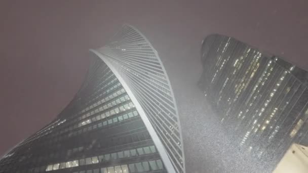 Rusland, MOSKOU - JANUARI 15, 2022: Wolkenkrabbers in sneeuwval 's nachts. Actie. Onderaanzicht van het bedrijfsleven hoogbouw in de moderne stad 's nachts in de winter. Prachtige wolkenkrabbers met 's nachts sneeuw. Moskou — Stockvideo
