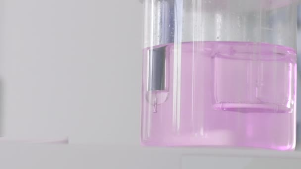 Primer plano del líquido rosa en recipiente transparente. Acción. Líquido rosado burbujeante en frasco transparente de laboratorio químico. Embutidos con líquido sobre fondo blanco — Vídeos de Stock