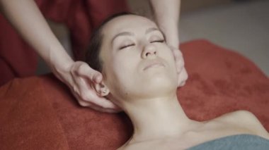 Genç ve çekici esmer kadın spa salonunda yüz ve kafa masajı yaptırıyor. Başla. Sağlıklı yaşam tarzı ve vücut bakımı kavramı.