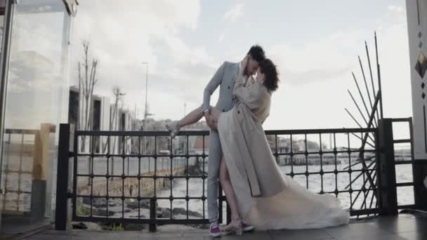 Bonita novia joven y elegante novio de pie al aire libre en un día ventoso. Acción. Una pareja casada posando delante de la cámara. — Vídeos de Stock