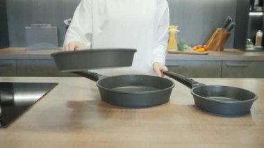 Beyaz üniformalı bir şef tarafından sunulan yeni kızartma tavaları. Başla. Modern bir mutfağın içinde..