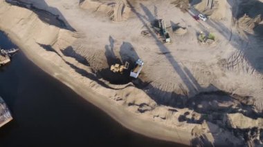 Fransa, Paris-26 Mayıs 2022: Sahne. Göletin yanındaki dağlık alanda çalışan büyük kamyon ve traktörleri görebileceğiniz kuş bakışı bir manzara. Yüksek kalite 4k görüntü