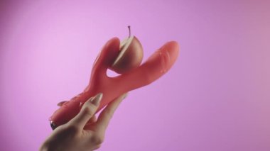 Nasıl çalıştığını göstermek için kadın eli ile kadın seks oyuncağını yarı elmayla tutarken yakın plan. Yaratıcı. Vibratör yüzeyindeki sıvı şeffaf kayganlaştırıcı pembe ve mor bir gradyan üzerinde izole edilmiş.
