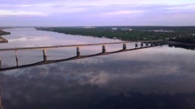 Gün batımında geniş nehrin üzerindeki uzun bir köprünün havadan görüntüsü. Şarjör. Köye yakın sakin bir nehri olan bir kırsal bölge.