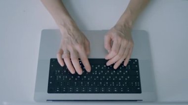 Eller klavyeye basıyor. Başla. Dizüstü bilgisayarın klavyesinde yazı yazan ellerin üst görüntüsü. Kişi minimalist tarzda yeni dizüstü bilgisayarda yazıyor.