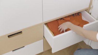 Sessizlik. Yaratıcı. İçinde eşyalar, kapüşonlular vs. olan küçük beyaz bir komodin. İstiflenmiş, açılmış ve giysiler çıkarılmış. Yüksek kalite 4k görüntü