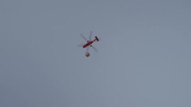 Helikopterin alttaki görüntüsünde askeri malzemeler uçarken barycentric kancadan sallanan bir iple asılıydı. Başla. Mavi gökyüzü arka planında uçan helikopter