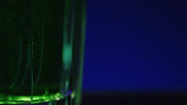 Bardakta köpükler olan yeşil içeceğe yakın plan. Borsa klipsi. Gece kulübünün arka planında yeşil içeceği bardakla tazeliyorum. Alkolik içki ve gece hayatı.