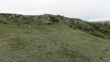 Bulutlu bir arka planda, yeşil yaz dağının tepesinde uçuyor. Vuruldu. Bir tepedeki yeşillik ve taşların havadan görünüşü