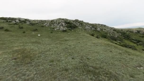 曇りの空の背景にある緑の夏の山の上を飛ぶ ショット 丘の上の緑と石の空想的な眺め — ストック動画