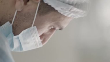  Ameliyathanede ameliyat yapan ve aşağı bakan bir cerrah. Başla. Hastanede maskeli ve şapkalı bir erkek doktor.