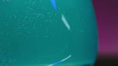 Pembe ışıklı arka plandaki açık mavi köpüklü içeceği kapat. Borsa klipsi. Gece barında eğlenme kavramı