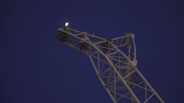 Çerçevede yük vinci var. Şarjör. Karanlıkta, vincin beyaz kısımları karanlık gökyüzüne karşı parlıyor. Akşam çalışan vinç yükleniyor.