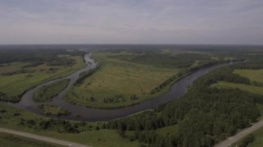 Akan bir nehrin havadan görünüşü ve geniş yeşil araziyi geçişi. Stok görüntüleri. Yeşil çayırı ve dar kıvrımlı nehri olan yaz kırsal arazisi
