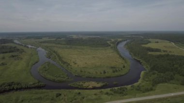 Akan bir nehrin havadan görünüşü ve geniş yeşil araziyi geçişi. Stok görüntüleri. Yeşil çayırı ve dar kıvrımlı nehri olan yaz kırsal arazisi