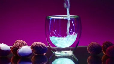 Mavi içki izole edilmiş arka planda bardağa dökülür. Borsa klipsi. Bardaki berrak bardağa karbonatlı mavi içecek dökülüyor. Orada meyveler ve malzemeler vardır.. 