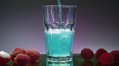 Mavi içki izole edilmiş arka planda bardağa dökülür. Borsa klipsi. Bardaki berrak bardağa karbonatlı mavi içecek dökülüyor. Orada meyveler ve malzemeler vardır.. 