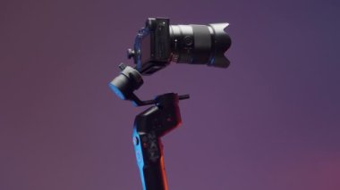 Aletlerle ateş etme kavramı. Eylem. Üzerinde büyük bir video kameranın olduğu büyük, yuvarlak bir üçayak. Parlak, mor bir arkaplanda farklı yönlere çekim yapıyor. Yüksek kalite 4k görüntü