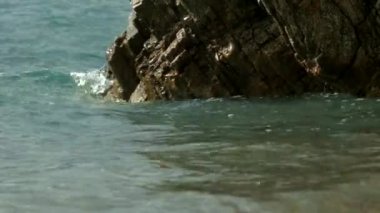 Denizi kokluyorum. Yaratıcı. Mavi şeffaf deniz dalgaları, yürüyen turistlerle dolu bir köprünün görüldüğü taşlara vuruyor. Yüksek kaliteli FullHD görüntüler