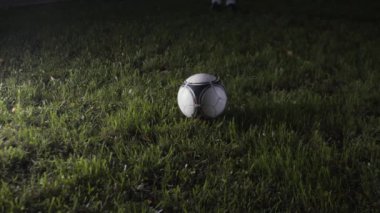 Çimlerin üzerinde futbol topunun yakın çekimi. Stok görüntüleri. Tek bir futbol topu yeşil çimlerin üzerinde yatıyor. Futbol topu çimlerin üzerinde gece ışıklarıyla yatar.. 