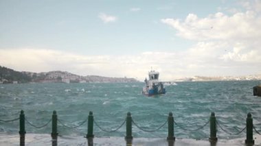 Deniz Burnu. Eylem. Üzerinde beyaz bir geminin yelken açtığı mavi dalgalı bir deniz ve sahilde küçük evleri olan bir şehir görülebilir. Yüksek kalite 4k görüntü