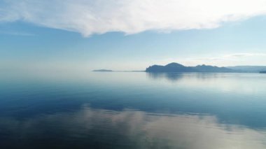 Temiz ayna gölü olan manzara. Vuruldu. Suya tepeden bakan mavi renkte manzara, uzaklıktan görünen dağlar ve yukarıda da sisli mavi bir gökyüzü görülebilir. Yüksek kalite 4k görüntü