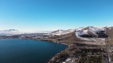 Büyük, koyu mavi bir göl, mavi gökyüzü ve karla kaplı dağların havadan panoramik görüntüsü. Görüntü. Resimli doğal vadi