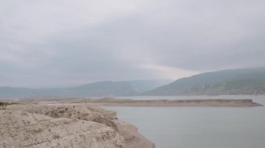 Sakin deniz suyu yüzeyi ve taş oluşumları. Başla. Mavi yaz denizi ve bulutlu bir arka planda çakıl taşı kıyısı