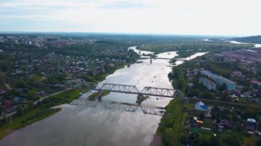 Şehrin havadan görünüşü ve köprüsü olan geniş bir nehir. Şarjör. Parlak bir arka planda, yaz şehrinin üzerinde uçuyor.