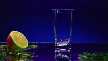 İçkili mavi arka plan. Borsa klipsi. Üzerine tarhun dökülen parlak bir zemin ve yanında köknar dalı olan bir limon. Yüksek kalite 4k görüntü