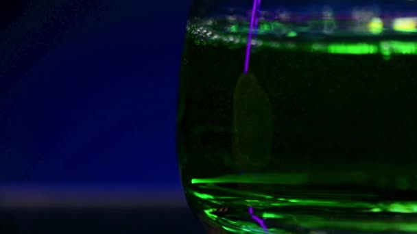 濃い青色の背景にあるグラスに緑色のドリンクを閉じます ストッククリップ カクテル付きのグラスのシルエット — ストック動画