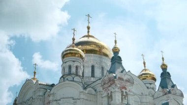 Ortodoks kilisesinin resimli görüntüsü. Şarjör. Yazın mavi gökyüzünün arka planında altın kubbeler olan güzel beyaz kilise. Güneşli bir günde altın kubbeli tarihi beyaz kilisenin alt manzarası. 