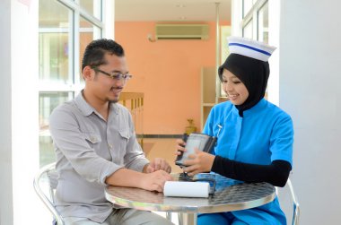 Confident Muslim patient checking blood pressure by nurse clipart
