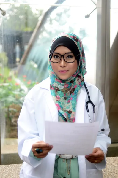 Jovem asiático muçulmano mulher médico na cabeça cachecol sorriso enquanto segurando relatório médico — Fotografia de Stock