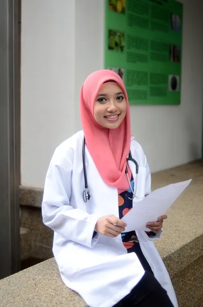 Jovem asiático muçulmano mulher médico na cabeça cachecol sorriso enquanto segurando relatório médico — Fotografia de Stock