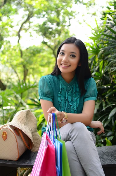 Beautiful shopping woman happy holding shopping bags take rest at garden and smile — Stock Photo, Image