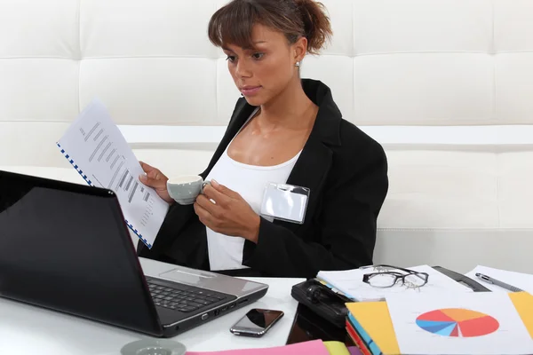 Businesswoman drinking coffee and looking at graphs — Stock Photo, Image