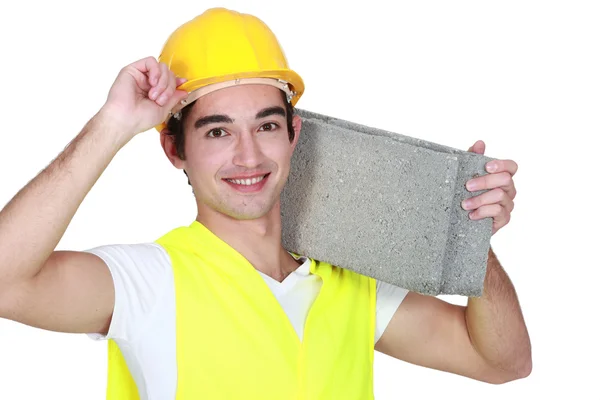 Jovem trabalhador da construção civil carregando um bloco de brisa . — Fotografia de Stock