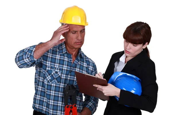 Verwirrter Handwerker beobachtet Ingenieur beim Schreiben auf Klemmbrett — Stockfoto