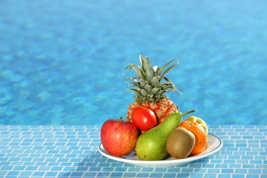 Plate of fruit next to a swimming pool clipart