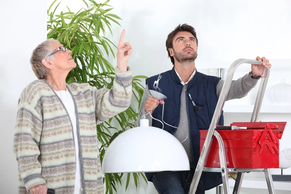 Man fixing ceiling light for old woman — Stock Photo, Image