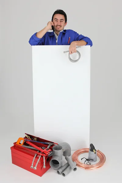 Encanador fazendo uma chamada enquanto está em pé por um painel de publicidade em branco — Fotografia de Stock