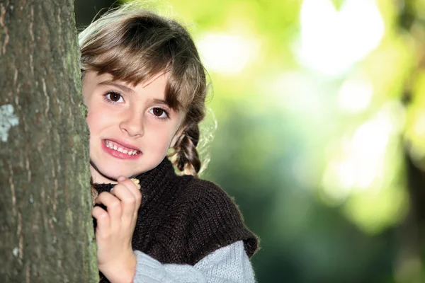 Young girl hiding behind a tree trunk — Stock Photo, Image