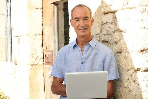 Homem sênior com laptop na frente da casa de pedra — Fotografia de Stock