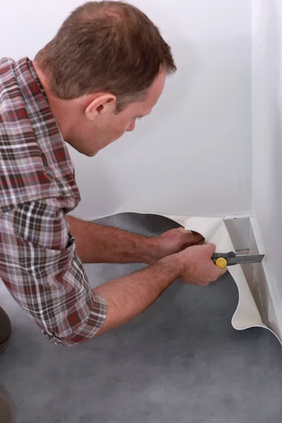 Handyman cutting linoleum flooring to fit a corner of a room — Stock Photo, Image