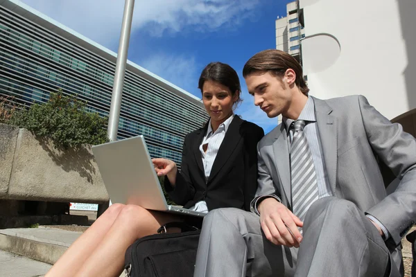 Pareja inteligente con un portátil fuera de un edificio corporativo — Foto de Stock