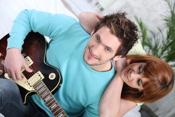 Casal sentado em um sofá com uma guitarra elétrica — Fotografia de Stock