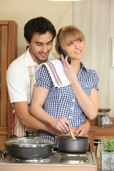 Jovem ao telefone enquanto cozinha o jantar — Fotografia de Stock