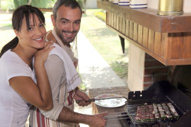 Couple cooking food on outdoor barbecue clipart