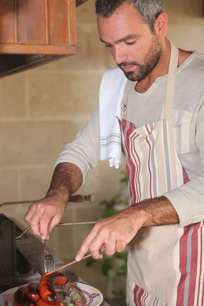 Homem na cozinha assar carne e salsichas de merguez — Fotografia de Stock